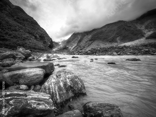 Dramatic perspective view in black and white from the Waiho River water level towards the track to Franz Josef Glacier located in Westland Tai Poutini National Park on the West Coast of New Zealand.