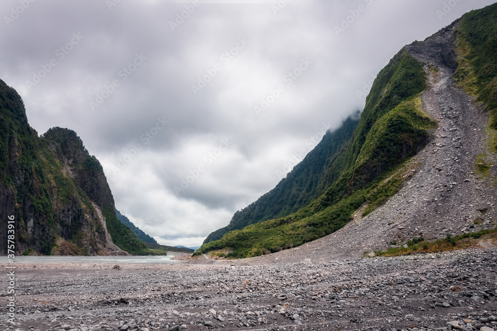Sheer green cliffs on each side of Waiho River Valley on the trail to Franz Josef Glacier in Westland National Park, Westland District, New Zealand. Panoramic view looking north-west.