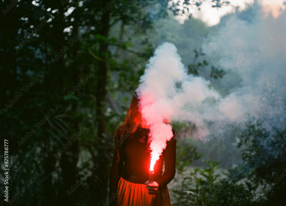 Woman holding a smoke bomb in front of her face the forest Woman holding a smoke bomb in front of her face the forest