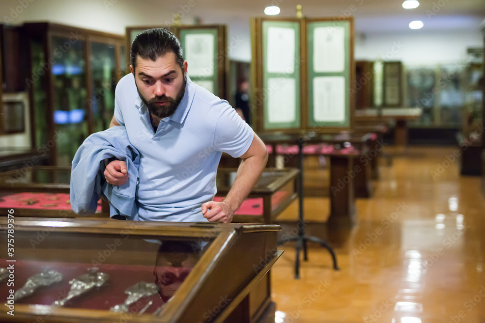 Fototapeta premium Adult man looking at exhibits in glazed stands in historical museum. High quality photo