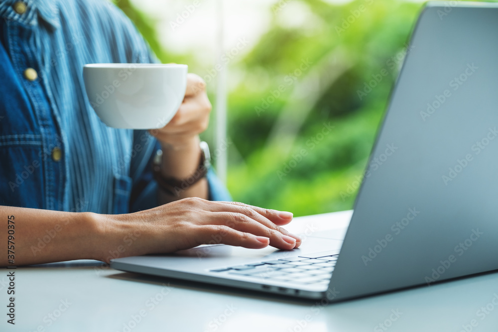 Closeup image of a woman working and touching on laptop computer touchpad while drinking coffee in office Closeup image of a woman working and touching on laptop computer touchpad while drinking coffee in office