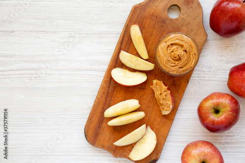 Raw Red Apples and Peanut Butter on a rustic wooden board on a white wooden background, top view. Copy space.