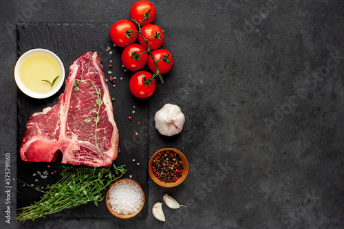  raw t-bone steak with ingredients on stone background with copy space for your text