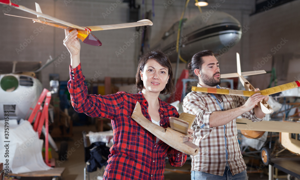 Portrait of happy female and male hobbyists with plane models created by them in aircraft workshop..