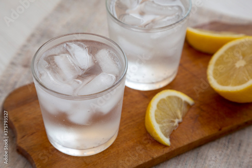 Fresh Lemon Sparkling Water with Ice on a rustic wooden board, side view. Close-up.