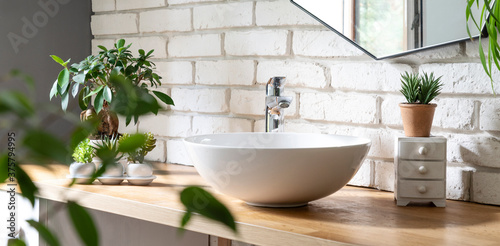 Bathroom sink. Stylish wash basin with faucet in industrial interior with white brick wall. Spa with green plants at home with mirror. Panoramic banner