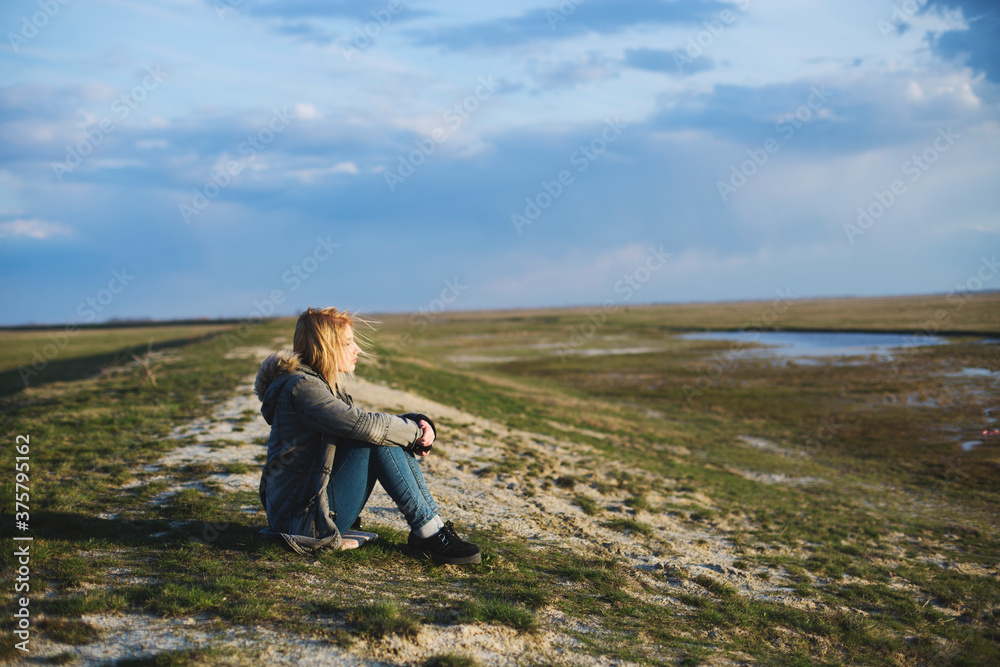 Young woman sitting on a hill with hair blowing in the wind Young woman sitting on a hill with hair blowing in the wind