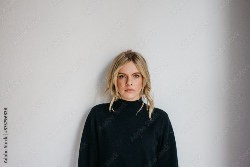 Young blonde female wearing dark sweater in front of white wall Young blonde female wearing dark sweater in front of white wall