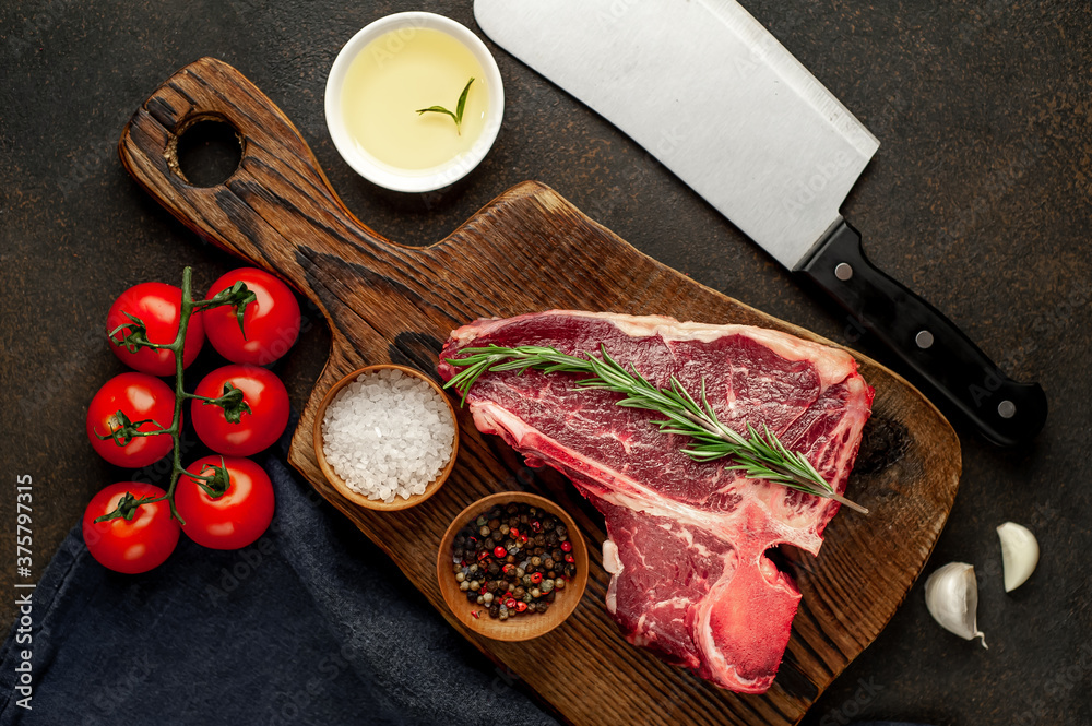 raw t-bone steak with ingredients on a wooden cutting board on a stone background raw t-bone steak with ingredients on a wooden cutting board on a stone background