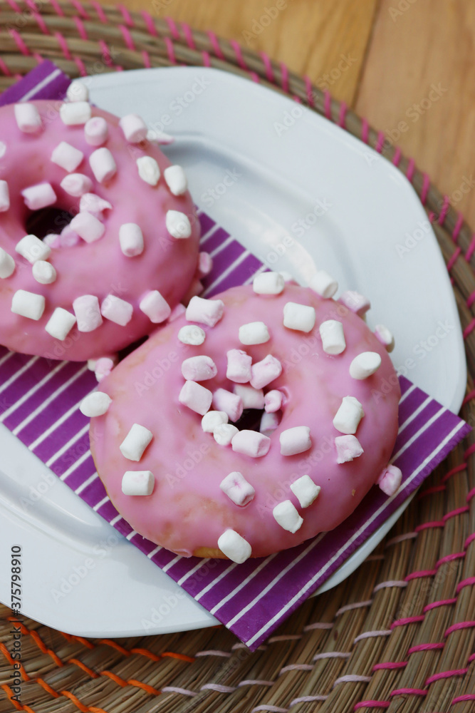 Pink glazed donuts with little marshmallow on a plate on wooden background Pink glazed donuts with little marshmallow on a plate on wooden background