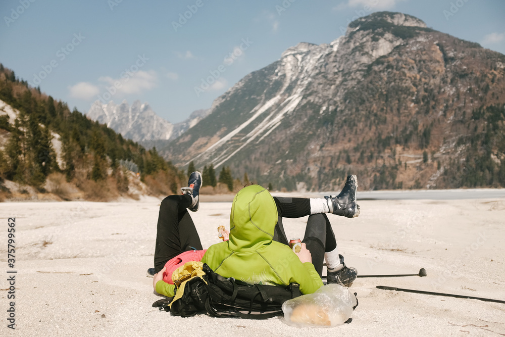 Man in hoody hugging his girlfriend while lying on sand beach in winter Man in hoody hugging his girlfriend while lying on sand beach in winter