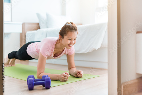 Healthy women in sportswear clothes is doing a plank exercise on yoga mat in bed room. Beautiful young woman exercises in home. 