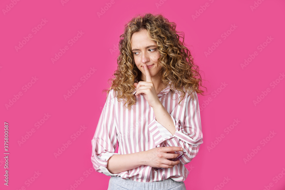 A young woman makes a gesture with her hands quietly, applying them to her lips.