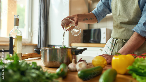 фотографія Cropped shot of man, Italian cook pouring a glass of white wine into the pan wit