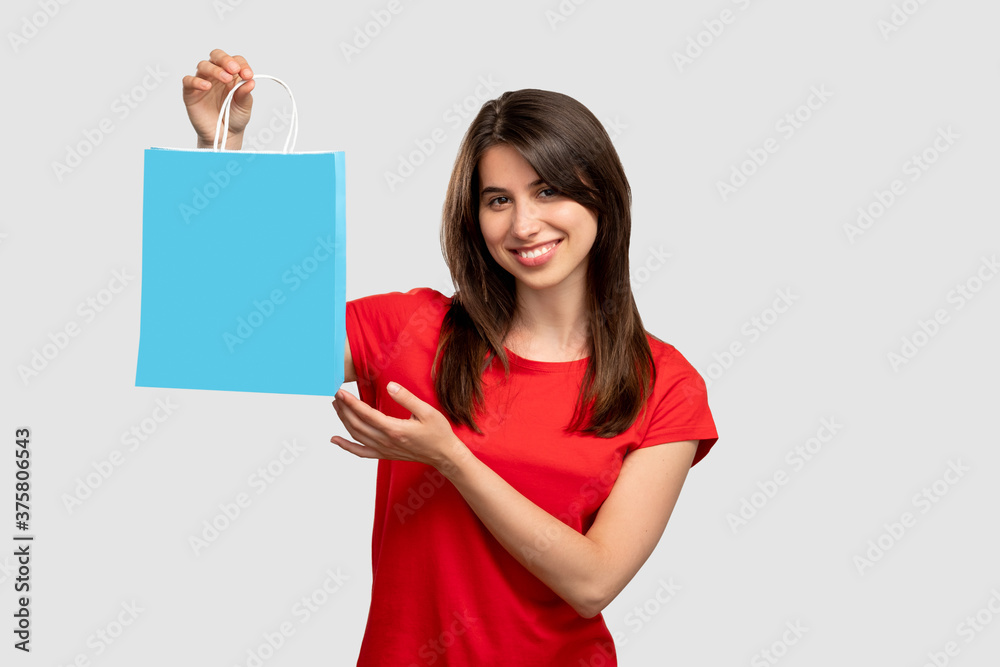 Holiday gift. Shopping bonus. Happy woman holding blue bag. Looking at camera isolated on neutral copy space. Sale and discount. Black friday. Advertising background Holiday gift. Shopping bonus. Happy woman holding blue bag. Looking at camera isolated on neutral copy space. Sale and discount. Black friday. Advertising background