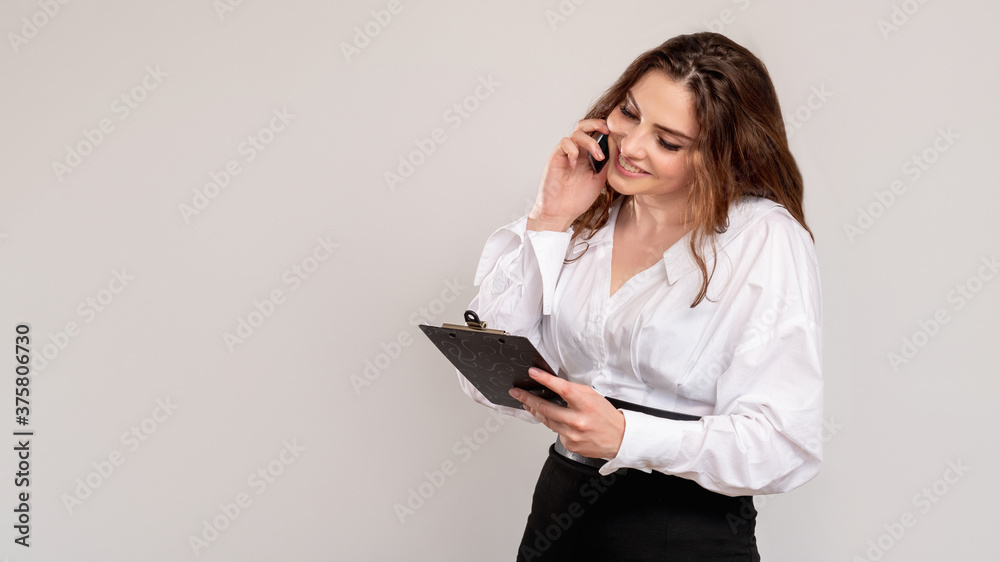 Ambitious woman. Business call. Confident smart female leader with clipboard discussing successful project on phone isolated on light copy space background. Professional communication. Ambitious woman. Business call. Confident smart female leader with clipboard discussing successful project on phone isolated on light copy space background. Professional communication.