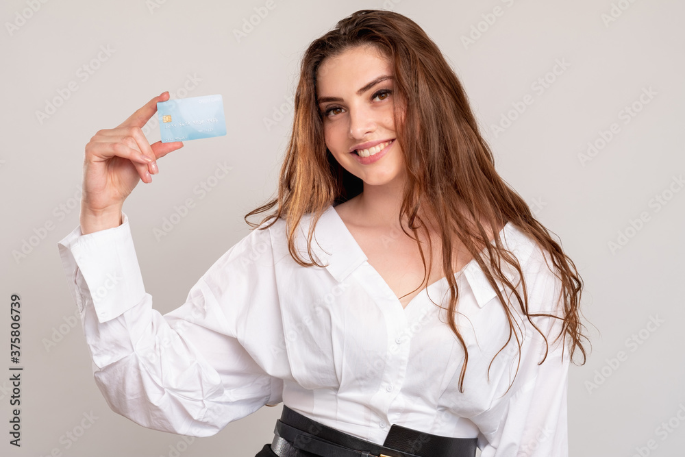 Contactless payment. Electronic money transfer. Cheerful woman in white shirt holding credit card isolated on neutral background. Personal data verification. Bank deposit. Contactless payment. Electronic money transfer. Cheerful woman in white shirt holding credit card isolated on neutral background. Personal data verification. Bank deposit.