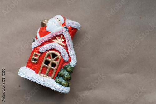 a small Christmas toy house in the snow with Santa Claus on the roof lies on a craft brown background Christmas toy on a brown background