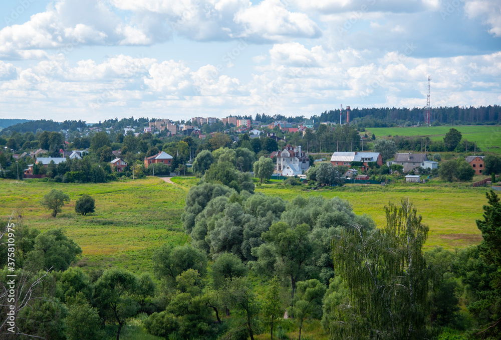 View from the hill to the fields, forest and village under a cloudy sky.