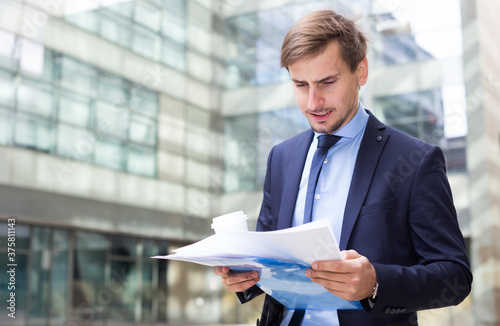 Professional man in jacket walking with coffee and watching documents