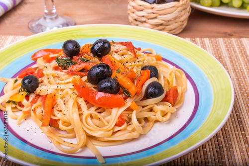 Classic Italian pasta with vegetables, linguine with sweet peppers, tomatoes and olives on a plate on a napkin on the table, close-up