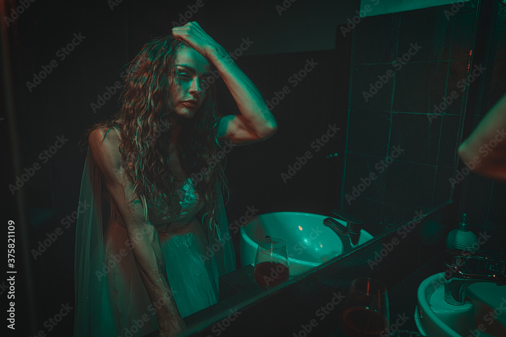 mysterious woman wearing wedding dress looking at her scary reflection in a mirror.