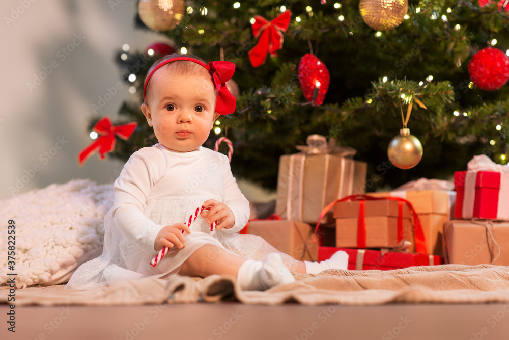 holidays and childhood concept - sweet baby girl at christmas tree with gifts at home