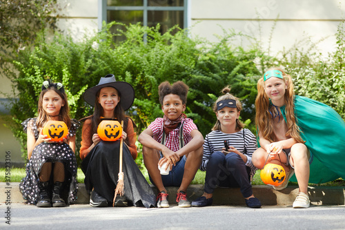 Group of children in Halloween costumes sitting on the ground and looking at camera they are at Halloween party