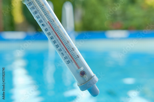 Thermometer measuring water temperature for swimming on a blurred background of blue water in the pool. Summer concept.