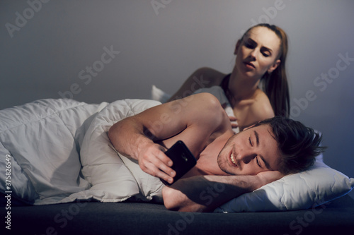 The concept of relationships and betrayal in the family. The man, lying in bed, corresponded on mobile phone with his mistress. The wife woke up and watching her husband