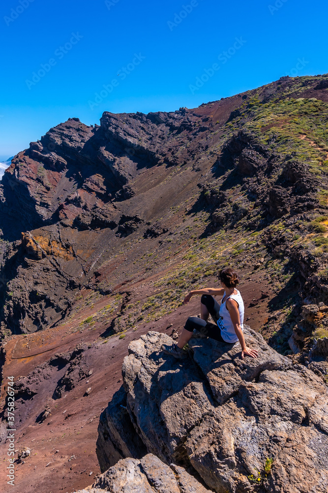 A young woman sits resting and looking at the views of the Roque de los Muchachos national park on top of the Caldera de Taburiente, La Palma, Canary Islands. Spain