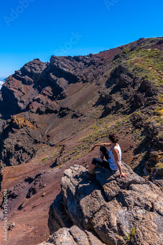 A young woman sits resting and looking at the views of the Roque de los Muchachos national park on top of the Caldera de Taburiente, La Palma, Canary Islands. Spain