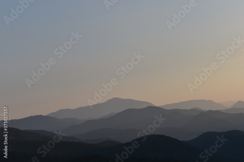 Weite Landschaft mit zum Horizont hin verschwimmenden Bergen und Hügeln in Abendstimmung, warme Farben 