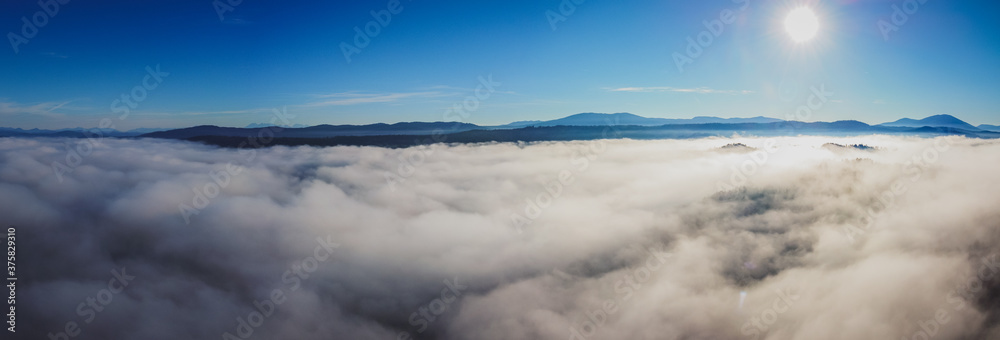 Obraz premium Early morning drone panorama of Planinsko Polje field in Slovenia during thick fog over the plain, with only higher hills such as Slivnica are seen sticking out.
