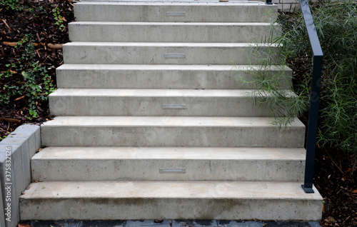 bright monolithic concrete park staircase with stair lighting with metal railing black interlocking paving, bushes slope photo