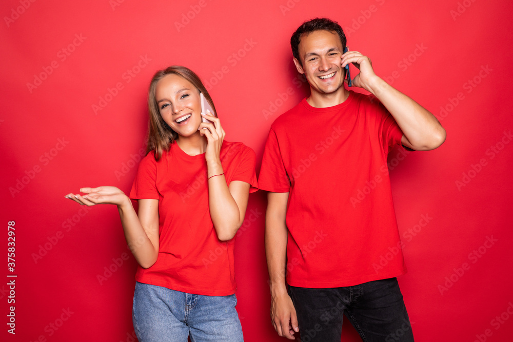 Obraz premium Attractive couple talking on their smartphones on red background