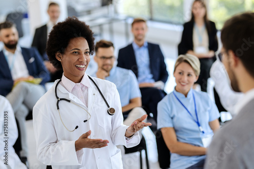 Happy black doctor talking to a presenter during an educational event at convention center.