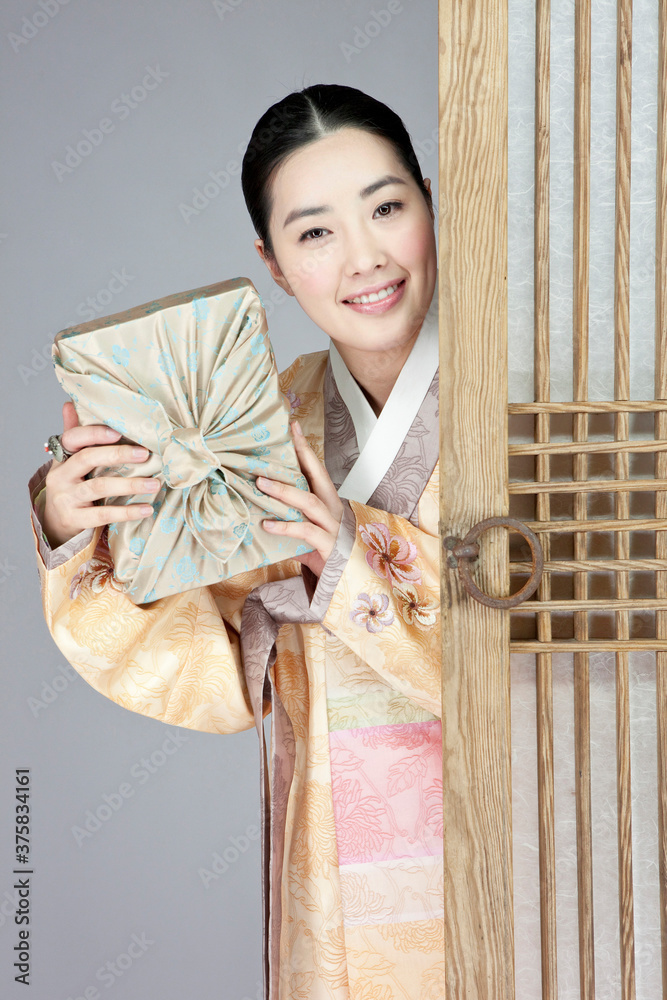 young woman in korean traditional clothing holding gift box hiding behind door young woman in korean traditional clothing holding gift box hiding behind door