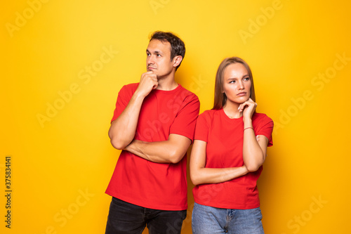 Young couple touching chin while looking aside isolated over yellow background