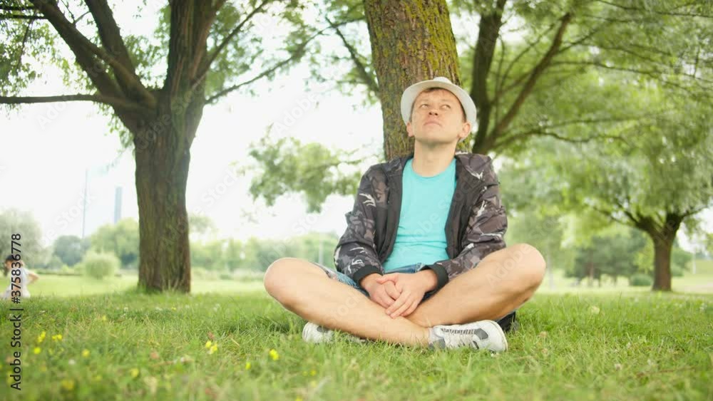 Handsome man resting while sitting under a tree, tracking by camera Handsome man resting while sitting under a tree, tracking by camera