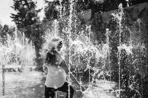 Black and white of the back of a woman with long hair running into a fountain. photo
