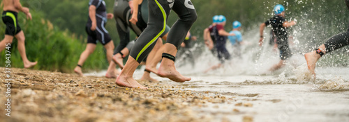 Fényképezés Legs of athletes in wetsuits running into a lake at a triathlon competition