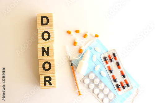 The words DONOR is made of wooden cubes on a white background with medical drugs and medical mask. Medical concept.