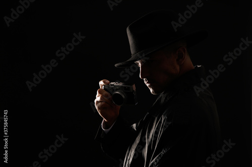 Old fashioned detective with camera on dark background. Space for text