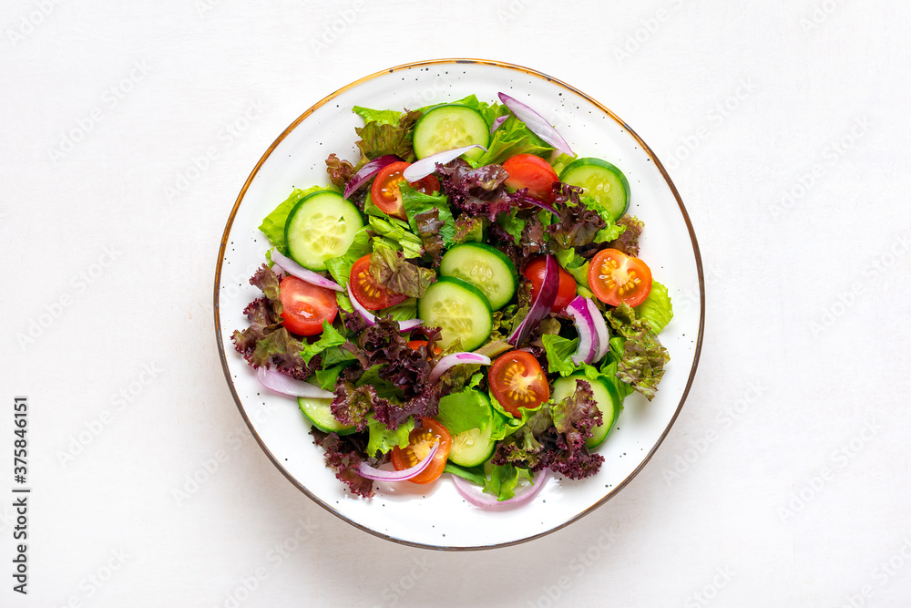 Healthy vegetable salad of red cherry tomatoes, cucumber slices, green and purple lettuce leaves, onions and olive oil in plate on white table Top view Flat lay Diet, mediterranean menu Vegan food