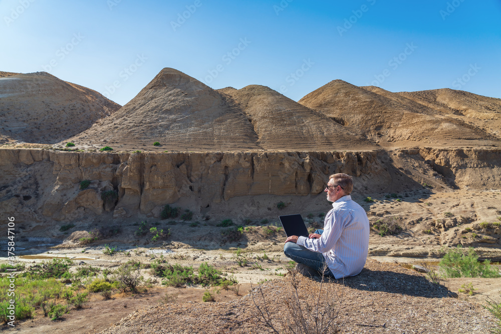 Traveler man working with laptop sitting on rocky mountain on beautiful scenic clif