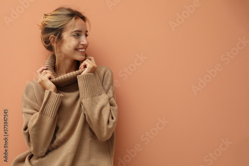 Beautiful young woman wearing knitted sweater on light brown background. Space for text photo