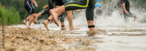 Athletes in wetsuits running into a lake at a triathlon competition photo