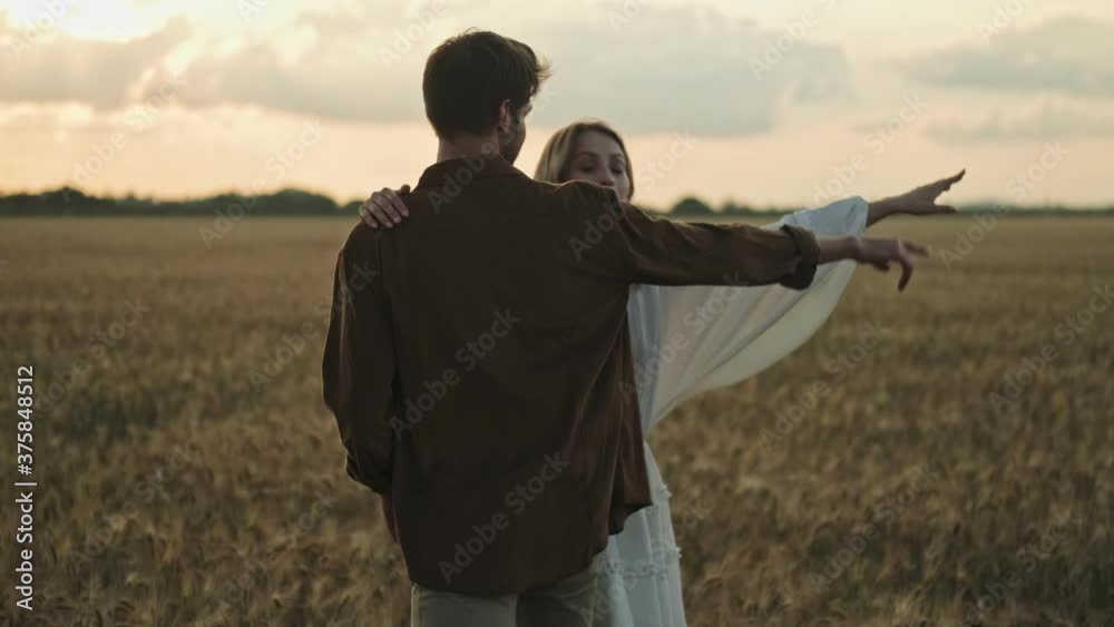 Young couple man and woman are looking and pointing to the side walking in the field Young couple man and woman are looking and pointing to the side walking in the field