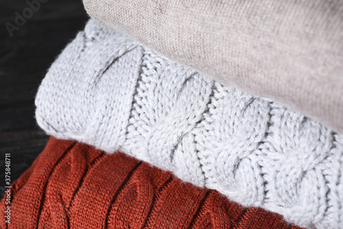 Stack of folded warm sweaters on black wooden table, closeup